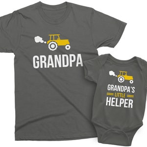 May include: A gray t-shirt with the text "Grandpa" and a yellow tractor graphic. A matching gray baby onesie with the text "Grandpa's Little Helper" and a yellow tractor graphic.