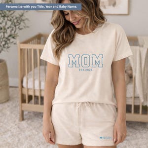 Peut inclure: Ensemble de pyjama cr&egrave;me compos&eacute; d'un t-shirt &agrave; manches courtes et d'un short. Le t-shirt affiche le mot "MOM" en lettres bleues soulign&eacute;es avec "EST.2026" en dessous. Le short a un cordon de serrage et le nom "NOAH" avec un c&oelig;ur.