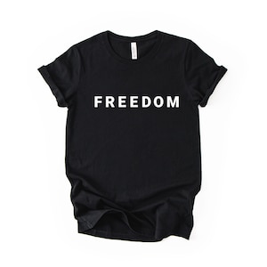 May include: Black t-shirt with the word "FREEDOM" printed in white block letters. The shirt has short sleeves and a crew neck. The fabric appears to be a soft cotton blend.