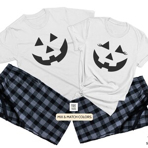 May include: A white t-shirt with a black jack-o'-lantern face graphic. The other t-shirt has a black jack-o'-lantern face with eyelashes. Both shirts are paired with black and gray plaid pajama pants. "Mix & Match Colors." is printed on the bottom of the image.