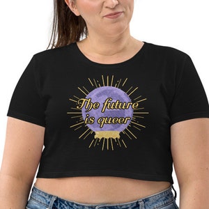 Può includere: Una maglietta nera a maniche corte e a taglio corto con una grafica viola e oro di una sfera di cristallo con il testo "The future is queer".