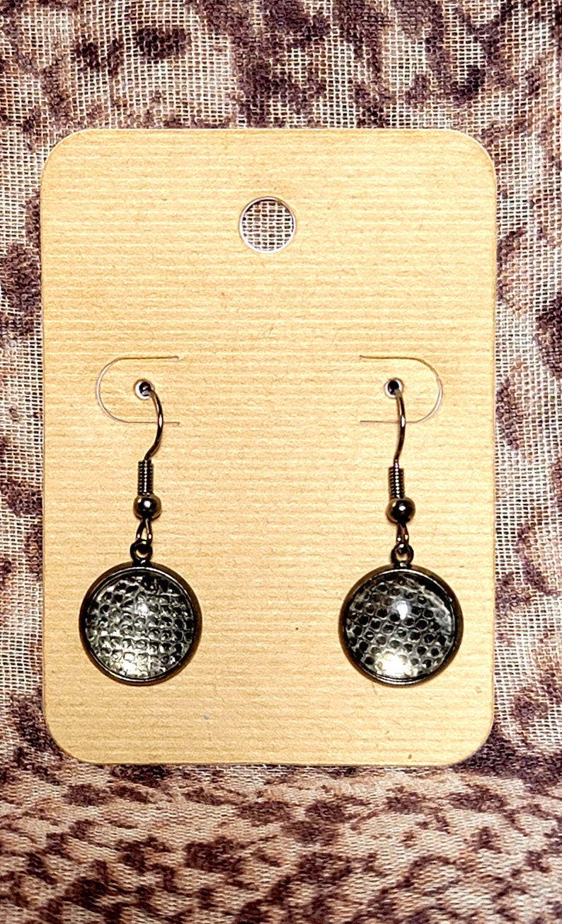 Puede incluir: Un par de pendientes de plata con colgantes redondos de vidrio. Los colgantes tienen un patr&oacute;n texturizado, como de panal de abeja.
