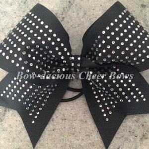 May include: Black cheer bow with silver rhinestones in a geometric pattern. "Bow-da-cious Cheer Bows" is printed on the bow.