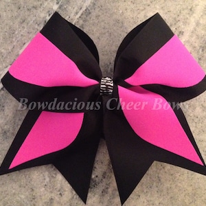 May include: A large black and hot pink cheer bow with a silver rhinestone in the center. The bow is made of two layers of ribbon and has a pointed shape.