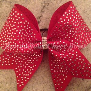 May include: A red cheer bow with silver rhinestones. The bow is tied with a silver elastic band.