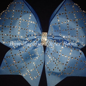 May include: A large blue cheer bow with silver rhinestones in a diamond pattern. The bow is tied with a silver ribbon.