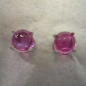 May include: A pair of silver earrings with pink gemstones. The gemstones are round and have a smooth, polished finish.