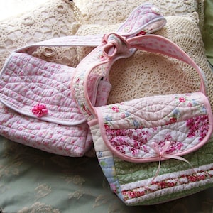 May include: Two quilted fabric handbags with floral patterns. The larger bag has a pink, green, and white striped design. The smaller bag is pink with white floral accents.