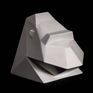 May include: A white, geometric sculpture of an animal head, possibly a lion or bear, against a black background. The sculpture has a faceted design with sharp angles and a smooth, glossy finish. The overall shape is angular and modern.