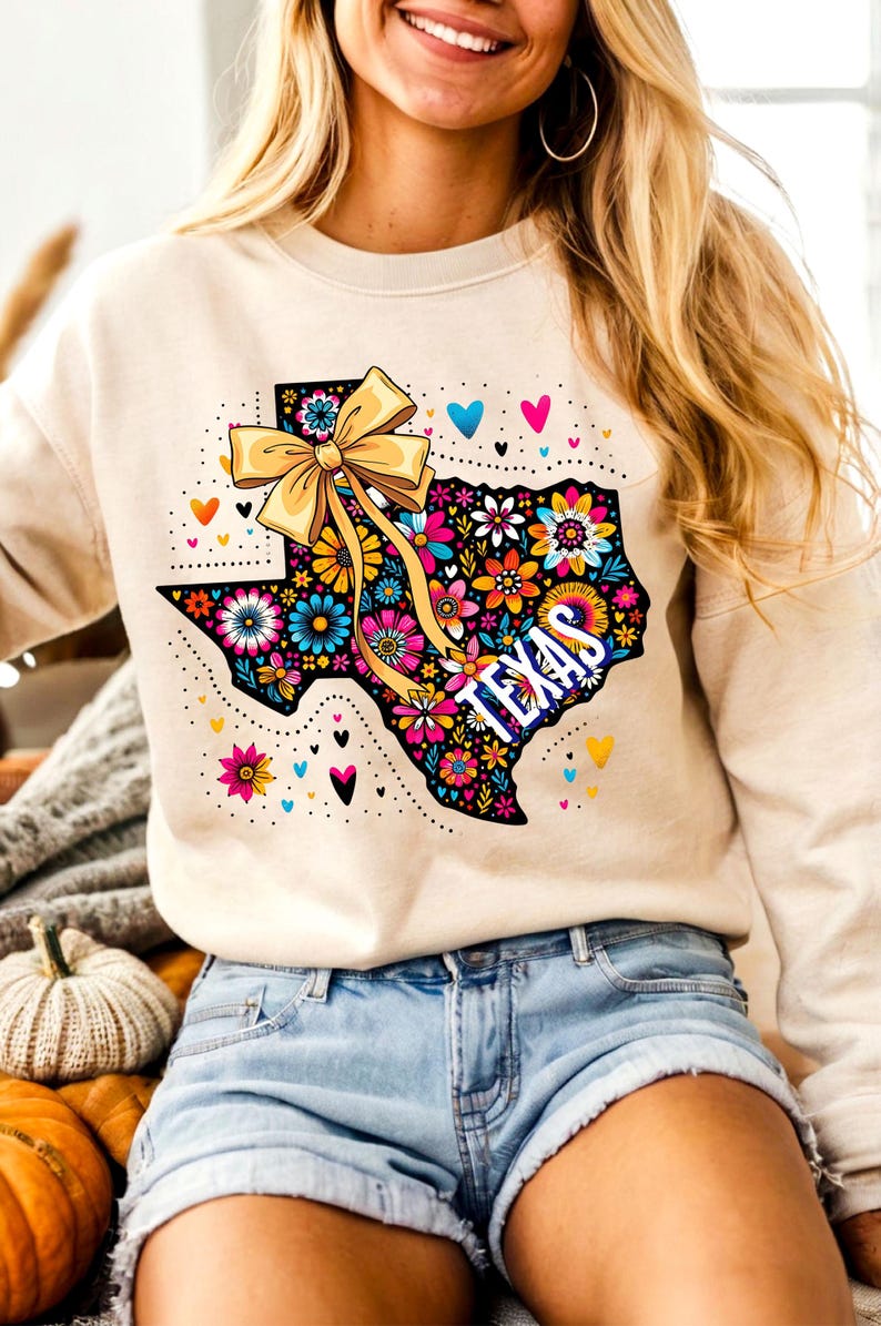 Puede incluir: Sudadera beige con un dise&ntilde;o floral colorido del estado de Texas, un lazo amarillo y la palabra "TEXAS". El dise&ntilde;o incluye corazones y detalles punteados. La sudadera se combina con pantalones cortos de mezclilla.