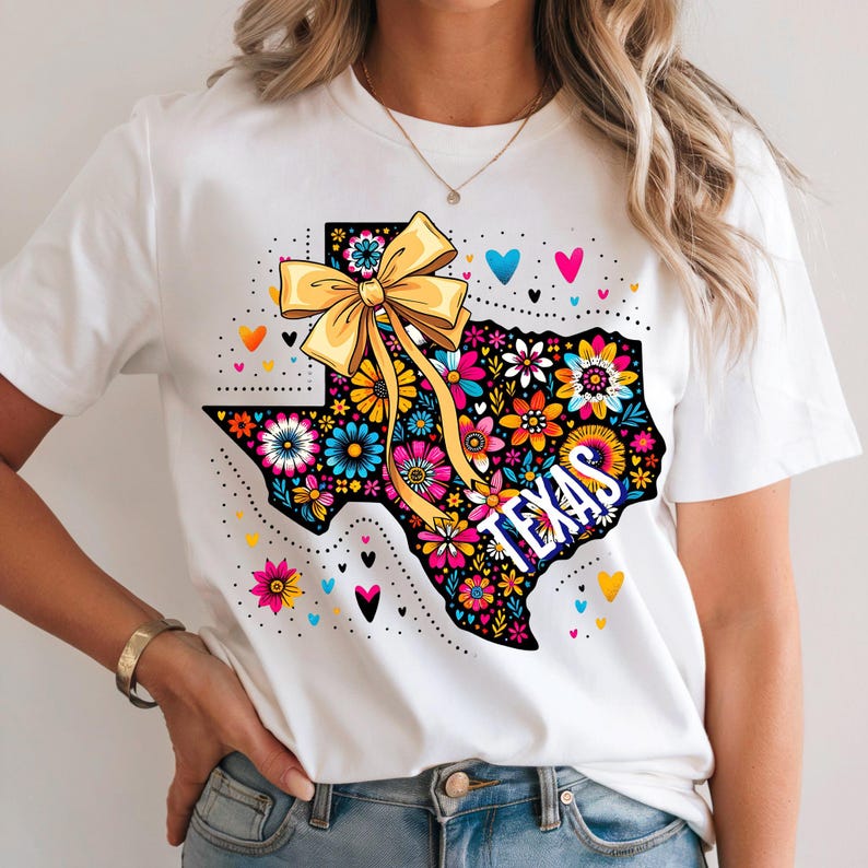 Puede incluir: Camiseta blanca con un dise&ntilde;o floral del estado de Texas. El contorno de Texas est&aacute; lleno de flores y la palabra "TEXAS". Un lazo amarillo y corazones completan el dise&ntilde;o.