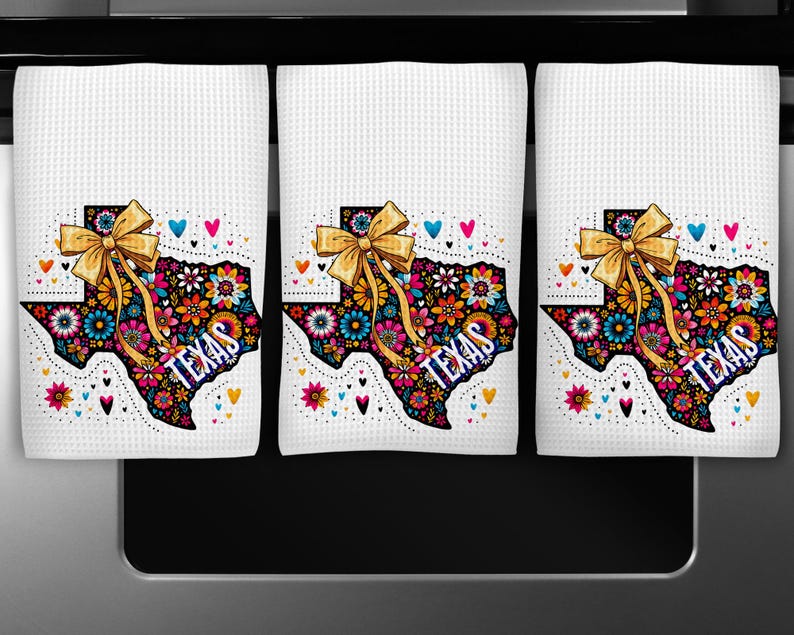 Puede incluir: Tres pa&ntilde;os de cocina blancos con un dise&ntilde;o en forma de Texas. El dise&ntilde;o presenta un colorido estampado floral, la palabra "TEXAS" y un lazo dorado. Corazones y flores de varios colores rodean el contorno de Texas.