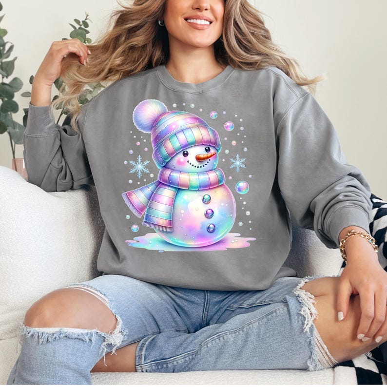 Puede incluir: Sudadera gris con un dise&ntilde;o de mu&ntilde;eco de nieve de dibujos animados colorido. El mu&ntilde;eco de nieve lleva un gorro y una bufanda a rayas, una nariz de zanahoria y ojos de bot&oacute;n. Copos de nieve y burbujas rodean al mu&ntilde;eco de nieve. Estilo casual.
