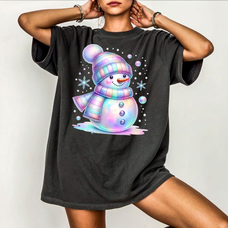 Puede incluir: Camiseta gris oscuro con un dise&ntilde;o de mu&ntilde;eco de nieve colorido y caprichoso. El mu&ntilde;eco de nieve lleva un gorro y una bufanda a rayas, con detalles de copos de nieve y burbujas. El dise&ntilde;o tiene un esquema de color arco&iacute;ris pastel.