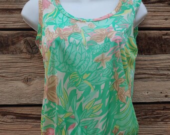 May include: A sleeveless, white tank top with a green, pink, and yellow floral print. The top has a scoop neck and a gathered hem.