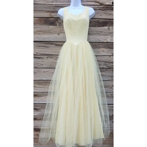 May include: A pale yellow tulle gown with a lace bodice. The gown has a fitted bodice and a full skirt. The gown is sleeveless and has a scoop neckline.