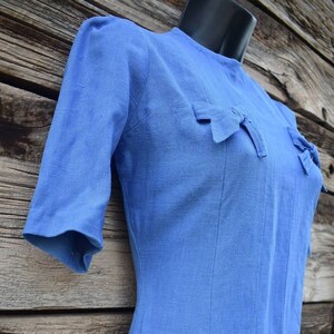 May include: A light blue linen dress with a fitted bodice and a-line skirt. The dress has a round neckline and short sleeves with bows on the shoulders.