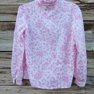 May include: A white blouse with a pink floral pattern. The blouse has a high neck and long sleeves.
