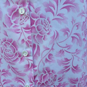 May include: A white button-down shirt with a pink floral pattern. The shirt has three white buttons down the front.