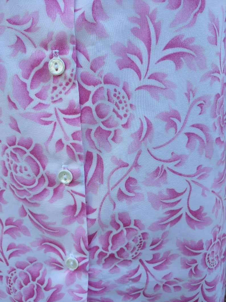May include: A white button-down shirt with a pink floral pattern. The shirt has three white buttons down the front.