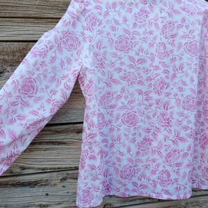 May include: A white long-sleeved shirt with a pink floral pattern. The shirt has a collar and long sleeves.