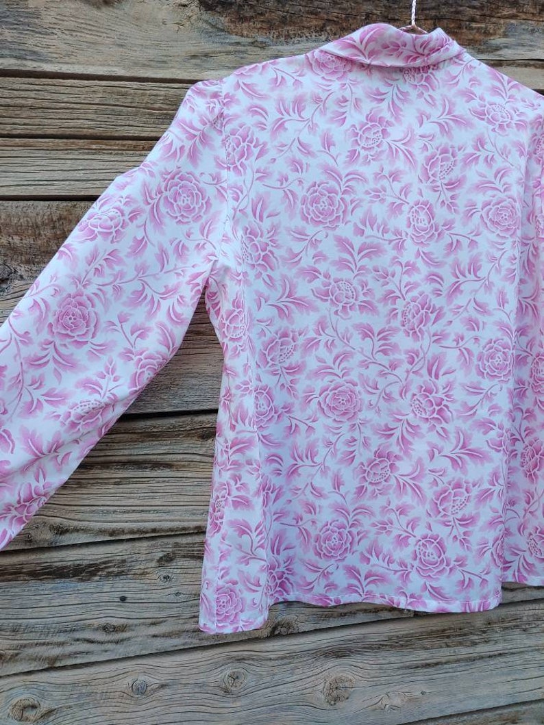 May include: A white long-sleeved shirt with a pink floral pattern. The shirt has a collar and long sleeves.