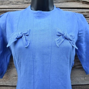 May include: A blue linen dress with a round neckline and short sleeves. The dress has two bows on the front, one on each side of the neckline.