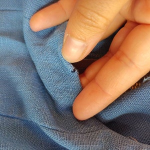 May include: Close-up of a blue fabric with a small tear in the material. A finger is shown pointing at the tear.