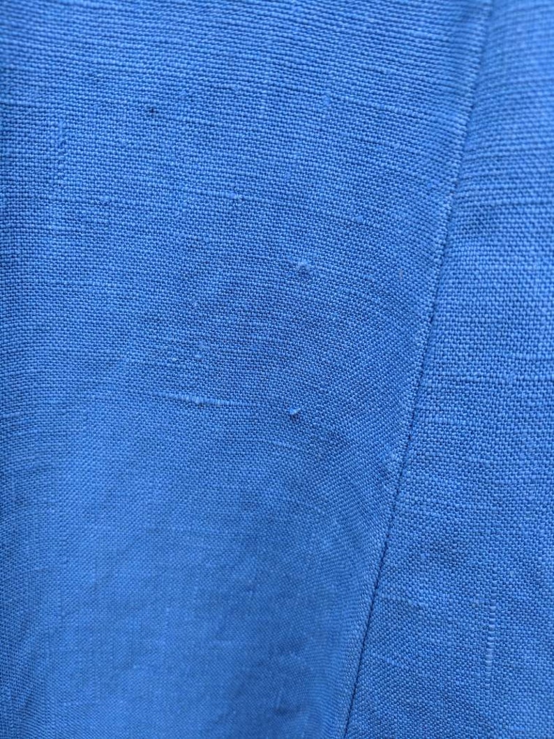 May include: Close-up of a blue fabric with a subtle texture. The fabric has a slight sheen and appears to be woven.
