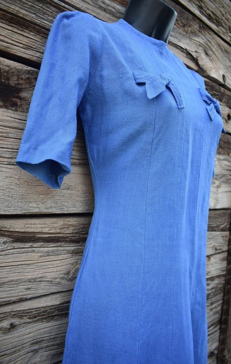 May include: A light blue linen dress with a fitted bodice and a-line skirt. The dress has a round neckline and short sleeves with bows on the shoulders.