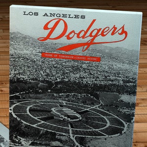 May include: A vintage Los Angeles Dodgers scorecard featuring a black and white aerial photograph of the Los Angeles Coliseum. The text "Los Angeles Dodgers" is in red lettering and the text "Home of Tomorrow - Chavez Ravine" is in smaller black lettering. The bottom of the scorecard is red and features a baseball graphic and the text "Official Dodger Score Card 20c".