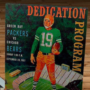May include: A vintage Green Bay Packers vs. Chicago Bears football game program from September 29, 1957. The program features a drawing of a player in a green and white uniform holding a football. The text "DEDICATION PROGRAM" is printed in orange at the top of the program. The price is 50 cents.