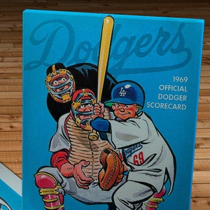 Może przedstawiać: Winietkowa karta punktowa meczu baseballowego Los Angeles Dodgers z 1969 roku z kreskówkową ilustracją łapacza i uderzającego. Karta punktowa jest niebieska z białym tekstem i kosztuje 25 centów.