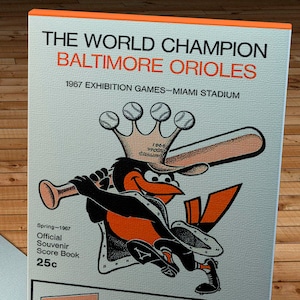 Könnte beinhalten: Ein Vintage-Souvenir-Spielbuch der Baltimore Orioles von den Ausstellungsspielen 1967 im Miami Stadium. Das Cover zeigt das Maskottchen des Teams, einen Baseballschläger, und den Text "The World Champion Baltimore Orioles". Enthält Werbung für Regal Premium Beer und Colt 45 Malt Liquor.