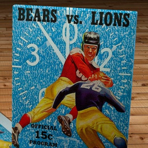 May include: A vintage sports program for a football game between the Bears and Lions. The program features a blue background with a clock face and two players in action. The text "BEARS vs. LIONS" is at the top of the program, and the text "WRIGLEY FIELD OCT. 13" is at the bottom. The program also includes the text "OFFICIAL 15c PROGRAM".