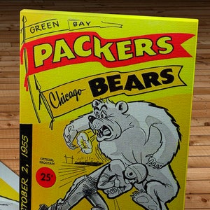 Może przedstawiać: Winietkowy program meczu futbolu amerykańskiego Green Bay Packers przeciwko Chicago Bears z 2 października 1955 roku w kolorze żółtym i czerwonym. Program zawiera rysunkową ilustrację niedźwiedzia atakującego piłkarza. Na programie nadrukowany jest tekst "OFFICIAL PROGRAM 25¢".