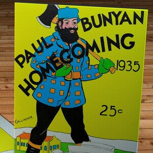 Op de afbeelding: Een canvas print met een vintage illustratie van Paul Bunyan met een bijl, in een blauwe jas met oranje vierkanten. De print toont de tekst "Paul Bunyan Homecoming 1935" en "Wisconsin vs Purdue". De prijs is "25¢".