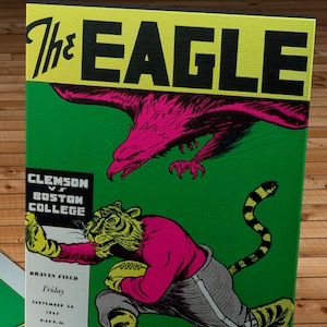 Pode incluir: Uma capa de programa vintage verde e amarela para um jogo de futebol americano entre Clemson e Boston College. A capa apresenta uma águia rosa com um tigre com um uniforme rosa e cinza segurando uma bola de futebol.