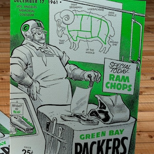 May include: A green and white illustrated poster advertising a Green Bay Packers football game. The poster features a cartoon butcher holding a cleaver and a ram with various cuts of meat labeled with football positions. The text reads "Special Today - Ram Chops" and "Green Bay Packers".