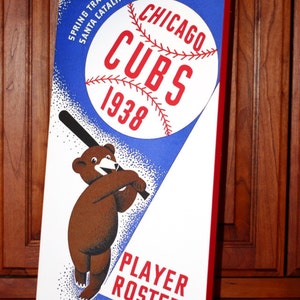 Könnte beinhalten: Ein Vintage-Poster für die Frühjahrstrainingsreise der Chicago Cubs 1938 nach Avalon, Santa Catalina Island, Kalifornien. Das Poster zeigt einen Comic-Bären mit einem Baseballschläger, einen Baseball mit dem Teamlogo und den Text "Chicago Cubs 1938 Player Roster".