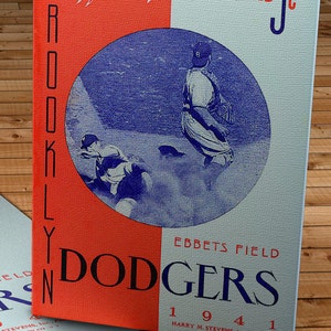 Może przedstawiać: Karta wyników Brooklyn Dodgers z 1941 roku, z ilustracją gracza w baseball w niebieskim okręgu na czerwono-białym tle. Karta zawiera tekst "Official Score Card" i "Ebbets Field".