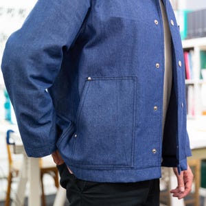 K&ouml;nnte beinhalten: Eine blaue Jeansjacke mit einer einzigen Brusttasche und mehreren silbernen Kn&ouml;pfen.