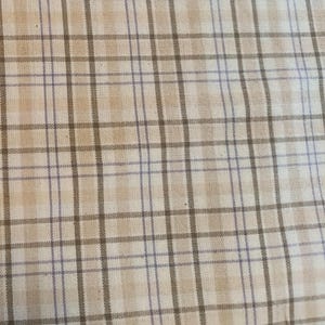 May include: Close-up of a beige and white plaid fabric with thin, dark brown and light purple lines. The fabric has a woven texture and a classic, timeless pattern, suitable for various textile projects.