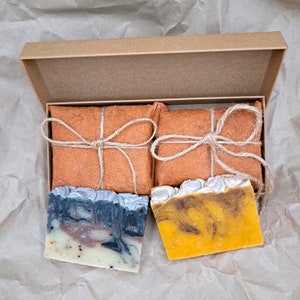 May include: Two bars of handmade soap wrapped in brown paper and tied with twine. One bar is a swirl of yellow and brown, the other is a swirl of gray and brown.