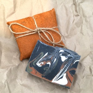 Pode incluir: Uma barra de sabonete artesanal com um design marmorizado preto, branco e marrom, embrulhada em papel castanho e amarrada com barbante.