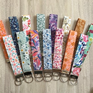 May include: A collection of 13 colorful fabric keychains with floral patterns. Each keychain has a silver metal ring.