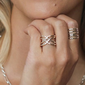 May include: A silver ring with a woven design. The ring is worn on the index finger of a person's hand.