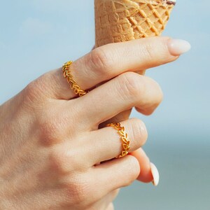 May include: A hand wearing two gold rings holds a waffle cone ice cream with chocolate pieces and a chocolate bar on top.