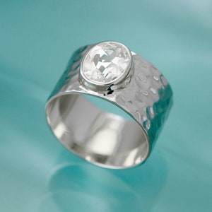 Op de afbeelding: Een zilveren ring met een gehammerde afwerking en een heldere ovale edelsteen.