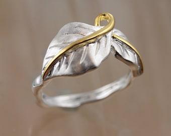 May include: A silver ring with a gold leaf design. The ring is made of two leaves, one on top of the other, with a gold band around the top leaf.